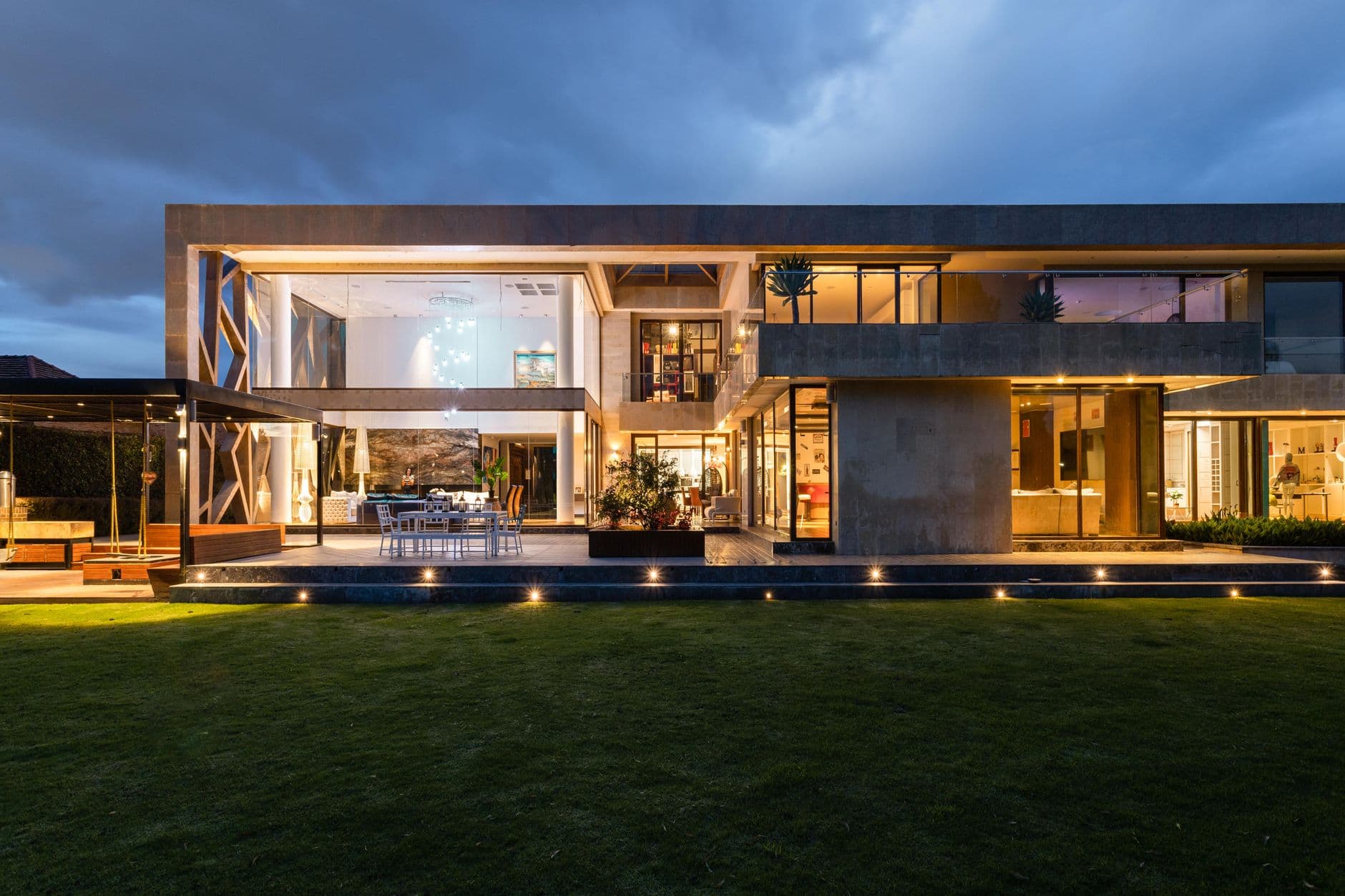 Long, low contemporary residence glowing from within at twilight, seen across a lawn