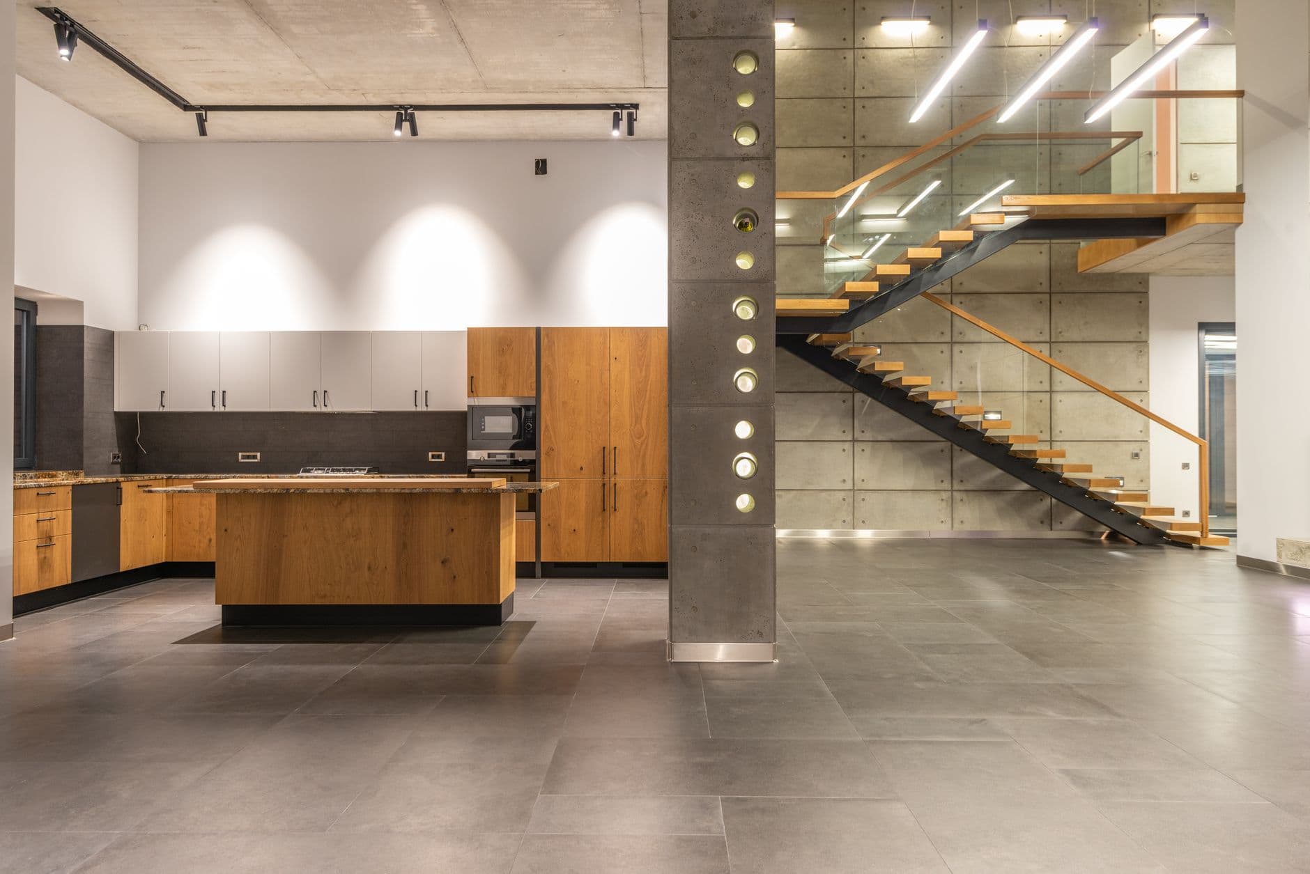 Open-plan kitchen in timber and stone beneath a steel and glass stair