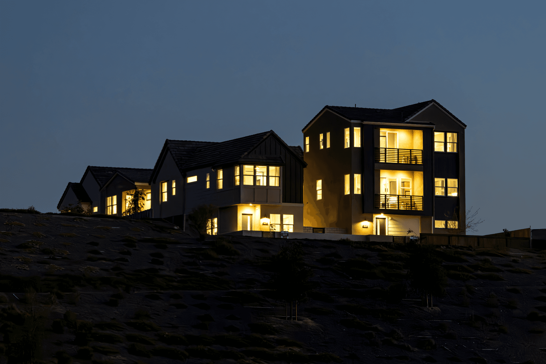 Dark-clad hillside residence with lit windows overlooking the valley at dusk