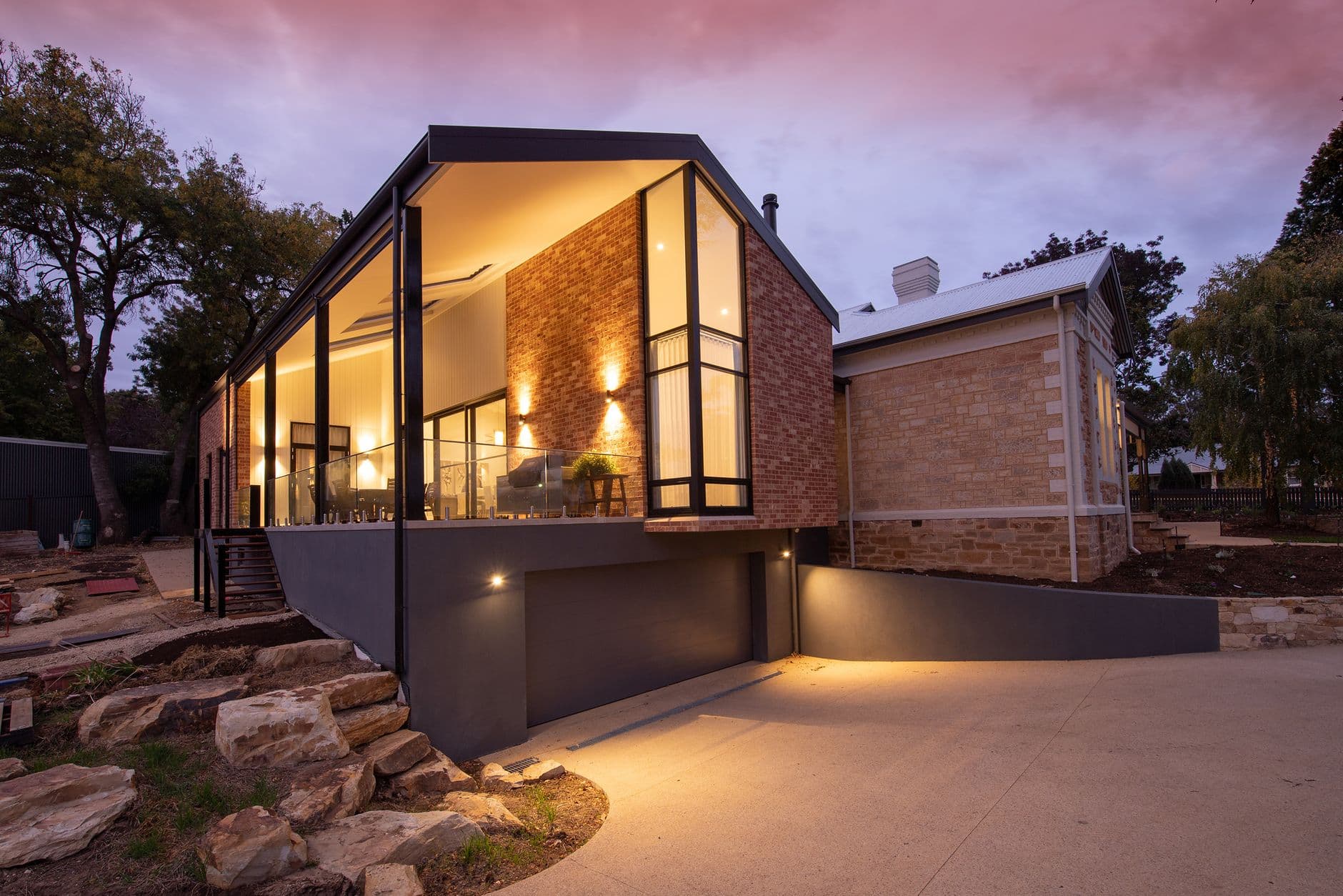 Modern gabled home in stone and glass, lit warmly against a dusk sky